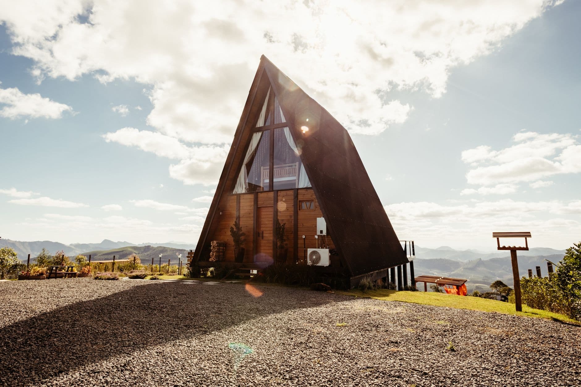 A wooden A-frame cottage against the backdrop of the Kazbegi mountains, surrounded by green meadows.