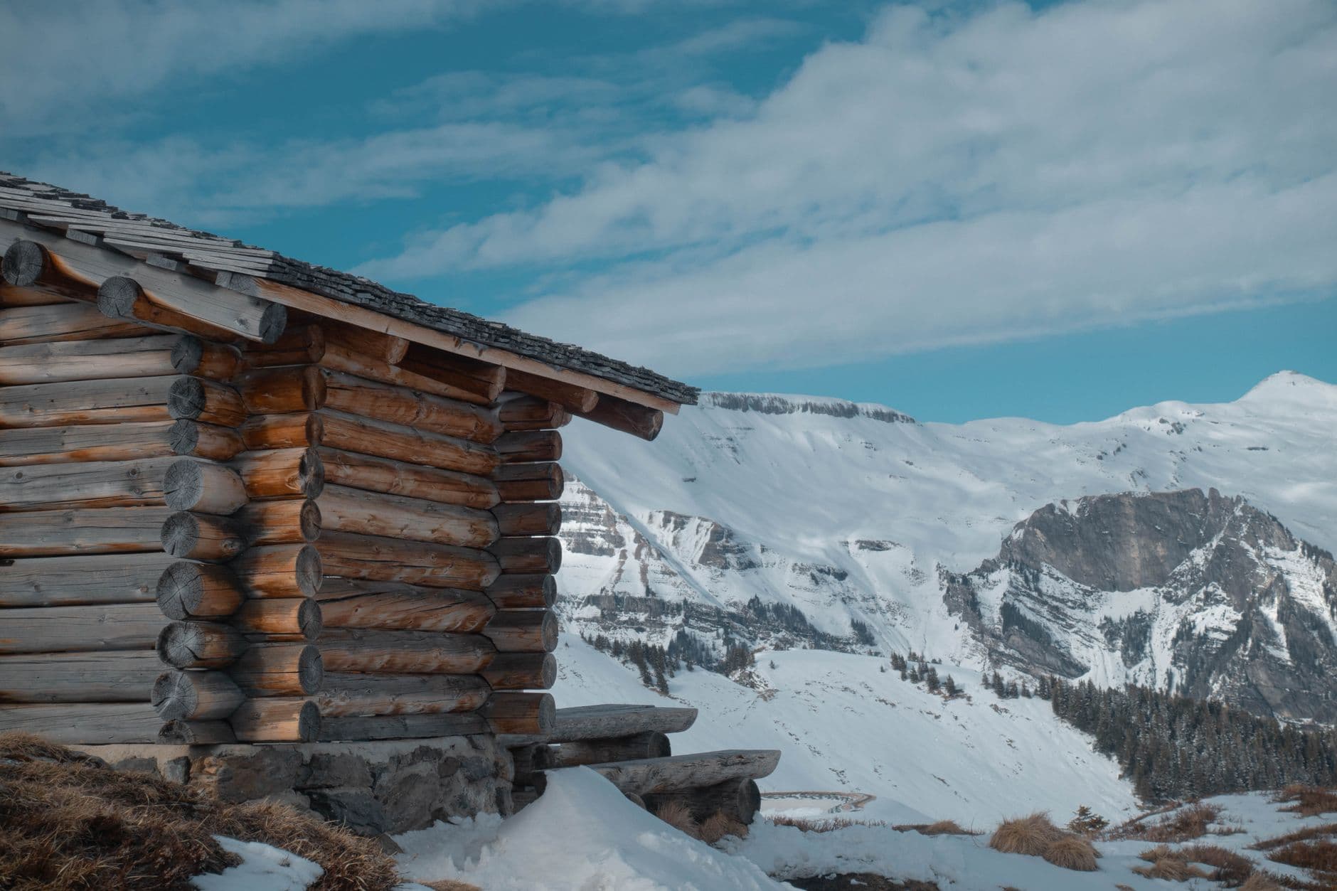 Snow-covered wooden cottage against the backdrop of the Caucasus Mountains on a sunny winter day