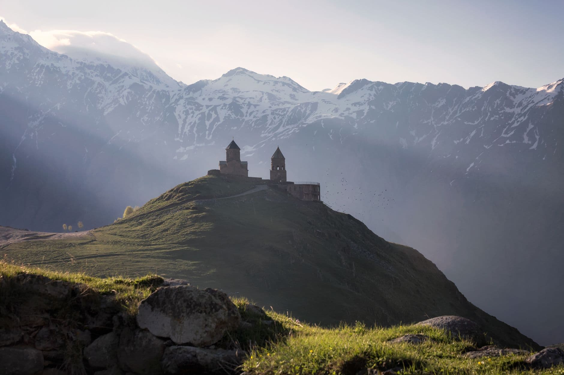 Gergeti Trinity Church against a backdrop of green mountains and a clear sky